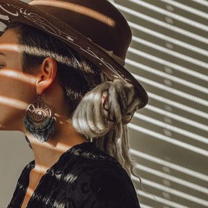 girl wearing wooden eye fringe earrings with brown hat