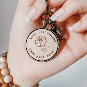 hand holding a keychain with floral girl and text reading "heal the trauma from your mama"